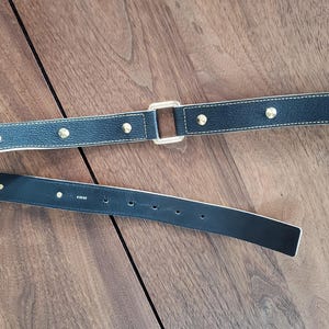 May include: A black leather belt with gold-toned hardware and a studded design. The belt is shown folded in half.
