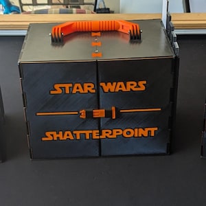 Puede incluir: Tres cajas de almacenamiento negras con asas naranjas y las palabras "Star Wars Shatterpoint" impresas en la parte delantera.