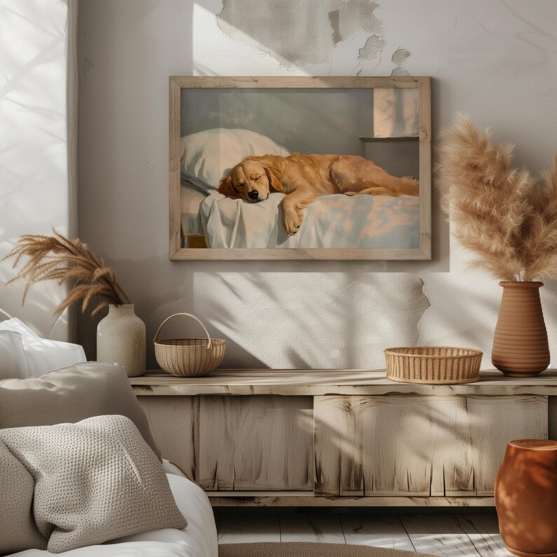 May include: A framed print depicts a sleeping golden retriever on a bed. The artwork is in a light wooden frame, and the dog is resting on a white pillow and sheet. The room has a neutral color palette with decorative vases and a woven basket.