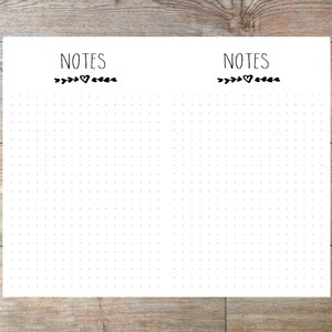 May include: White notepad with a dotted grid pattern. The word "NOTES" is printed at the top, above a decorative heart and leaf design. The notepad is on a wooden surface.