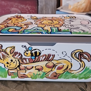 May include: A white storage box with a gray lid. The box is decorated with a colorful cartoon scene of a giraffe, a lion, an elephant, and bees. The word "CAL" is written in green letters on the lid.