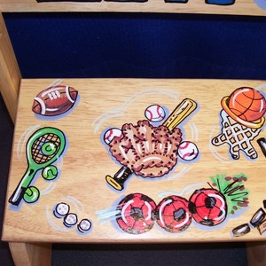 May include: A wooden chair with a painted design of various sports equipment, including a baseball glove, bat, basketball, football, tennis racket, and soccer balls.