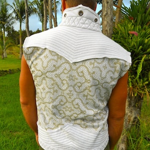 May include: A white sleeveless vest with a quilted design and a geometric pattern in gold. The vest has a high collar and a button closure.