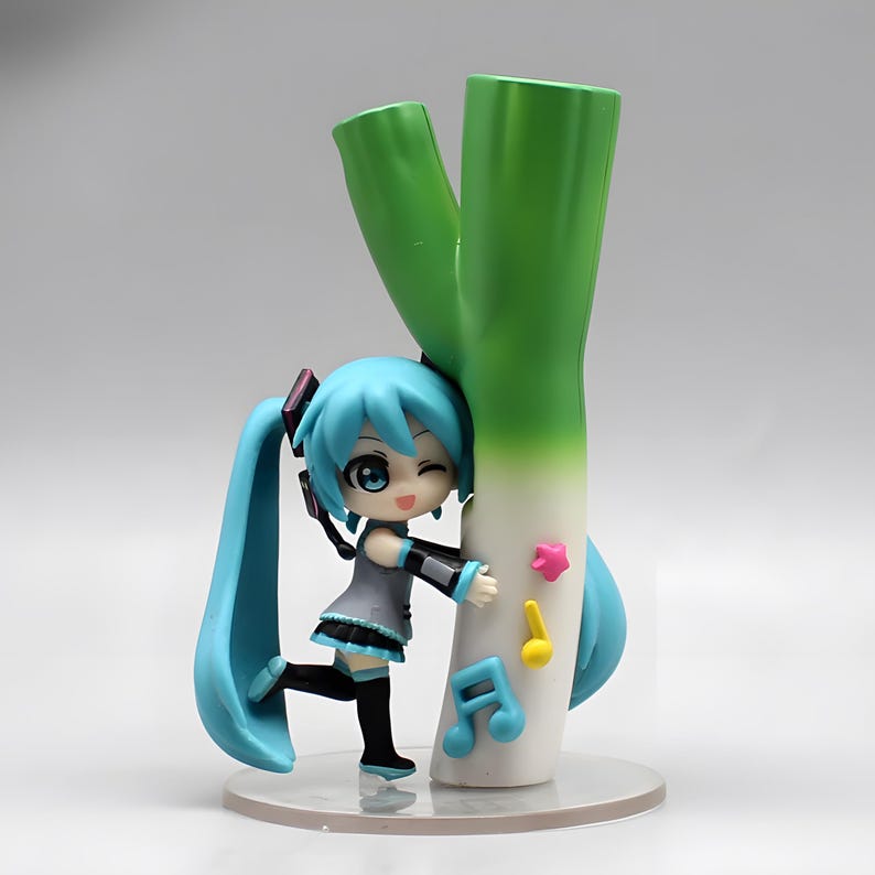 May include: A figurine of a character with turquoise hair and a grey dress, hugging a large green and white vegetable. The figurine has black accents and is posed with a wink. Musical notes and a star are attached to the vegetable.