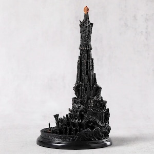 May include: A detailed black sculpture of a tall tower with intricate architectural details. The tower has a textured surface and a small, orange-colored element at the top. It sits on a round, black base.