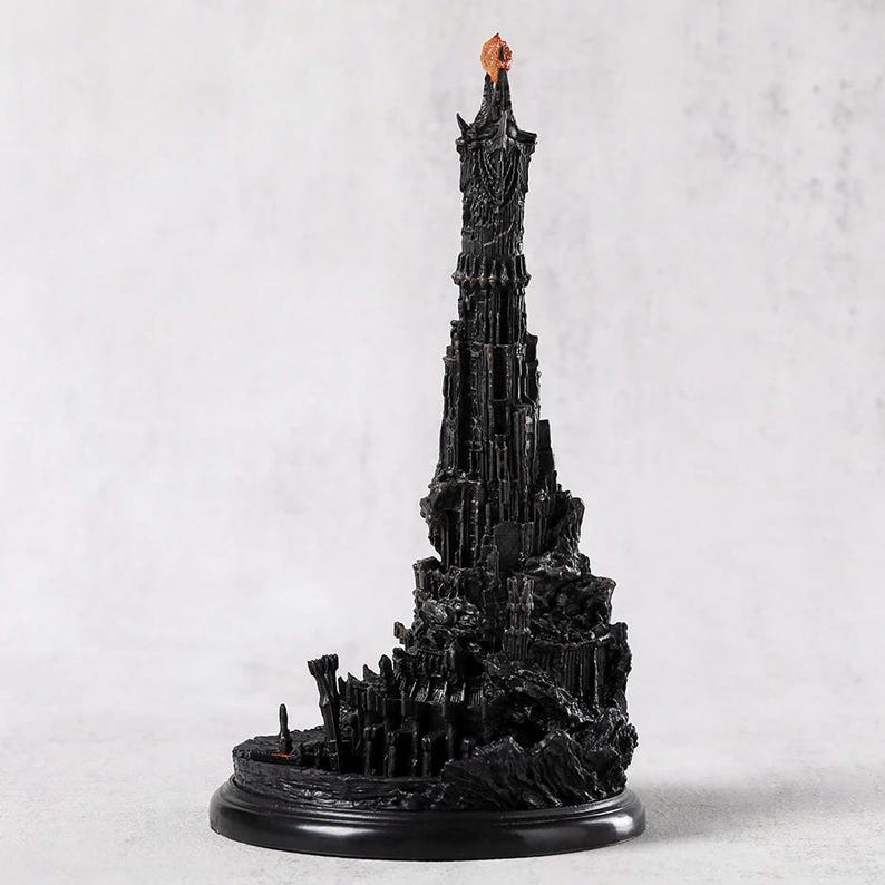 May include: A detailed black sculpture of a tall tower with intricate architectural details. The tower has a textured surface and a small, orange-colored element at the top. It sits on a round, black base.