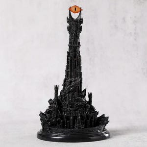 May include: A black, detailed sculpture of a tall tower with an orange eye at the top. The tower has intricate architectural details and sits on a round base. The eye is a prominent feature, adding a striking contrast to the dark structure.