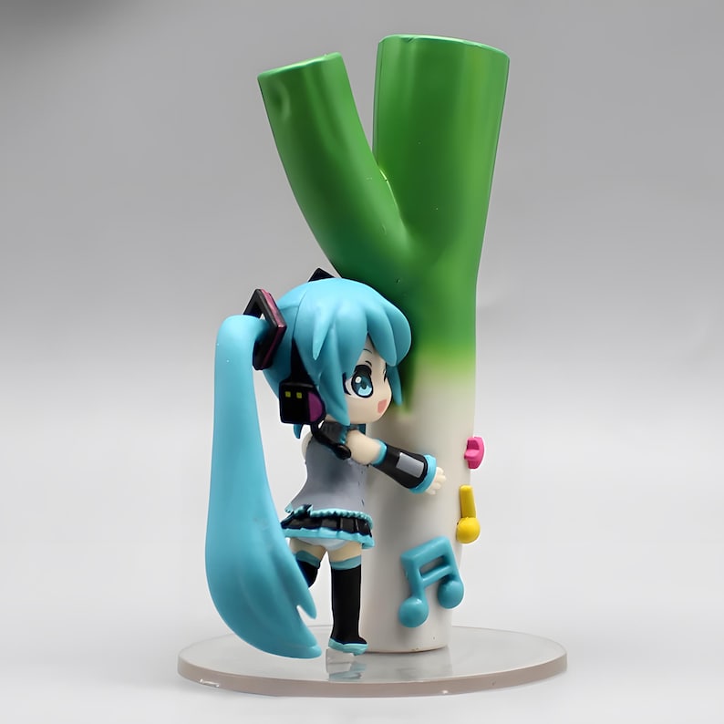 May include: A figurine of a blue-haired anime character with headphones, leaning against a large green and white leek. The figurine has a gray top, black skirt, and black boots. Musical notes are attached to the leek.