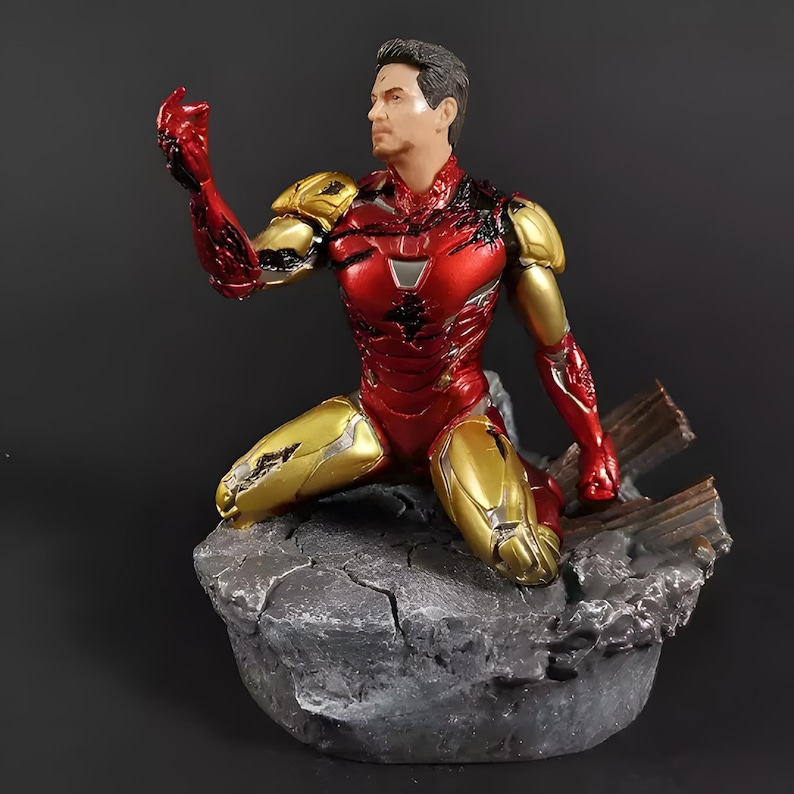 May include: A red and gold Iron Man action figure in a kneeling pose, with a damaged suit and a distressed base. The figure is made of plastic and has a detailed paint job.