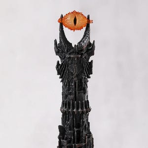 May include: A black tower with an orange eye at the top. The tower has a detailed, textured surface. The eye is orange with a black pupil. The overall design is reminiscent of a fantasy theme.