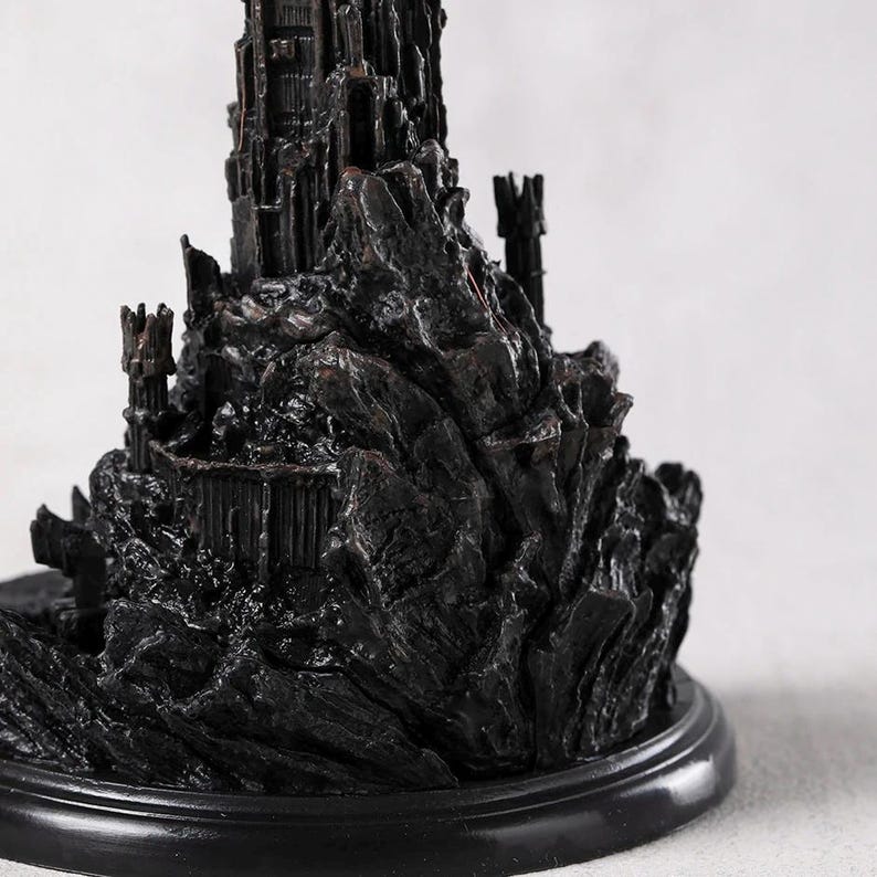 May include: A detailed, dark-colored miniature castle sculpture. The castle features intricate architectural details, including towers, walls, and a rocky base. The sculpture is mounted on a round, black base, and the overall aesthetic is gothic and imposing.