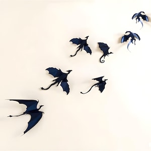 Könnte beinhalten: Ein Set aus sieben schwarzen Papierschatten von Drachen, jede mit einer einzigartigen Pose, sind diagonal an einer weißen Wand angeordnet.