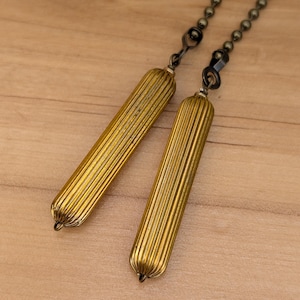 May include: Two antique brass-colored ceiling fan pull chains. Each pull features a ribbed, cylindrical design with a small loop at the bottom. The chains are attached to a dark metal ball chain.