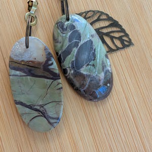 May include: Two decorative ceiling fan pulls. One is a polished, oval-shaped stone with green and brown veining. The other is a similar stone with a leaf-shaped metal accent. Both are attached to brass-colored chains.