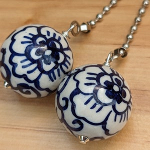 May include: Two white ceramic fan pull chains with blue floral designs. The chains are silver and have a loop at the top.