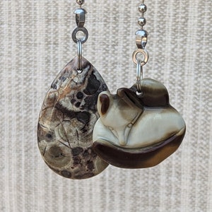 May include: Two decorative fan pull chains. One is a teardrop shape with a brown and tan patterned stone. The other is a round shape with a carved fox design in shades of brown and white.