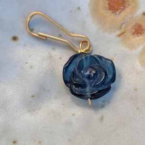 May include: A dark blue glass rose bead attached to a gold-toned metal wire hook. The rose features intricate, molded petal details and a translucent finish. The metal hook is shaped like a safety pin or clasp, providing a secure attachment point.