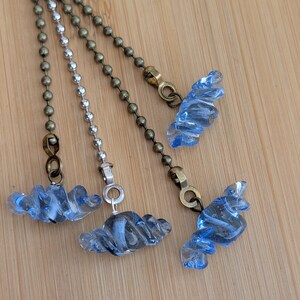May include: Three ceiling fan pull chains featuring light blue, twisted glass bead ornaments. Two chains are finished in an antique brass tone, while the center chain features a silver-toned metal finish. Each pull is attached to a metal connector.
