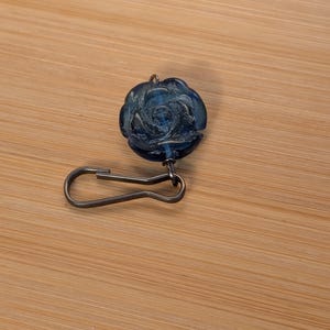 May include: A blue glass rose charm with a silver metal clip. The charm is a decorative element for jewelry or crafts.