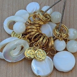 May include: A collection of white shell and gold-toned metal charms, including a ring, a circle, and a flower design. The charms are strung together with a brown twine.