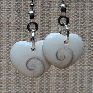 May include: Two white heart-shaped shell pendants with a spiral pattern hanging from silver chains.