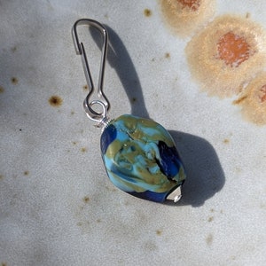 May include: A silver metal clip with a blue, gold, and white glass bead attached. The bead has a swirled pattern.