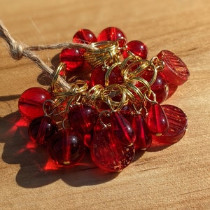 May include: A bunch of red glass beads with gold metal rings, strung together with twine. The beads are various shapes, including round, teardrop, and faceted.