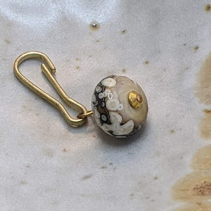 May include: A gold-toned metal clasp attached to a round, white and brown agate bead with a gold accent.
