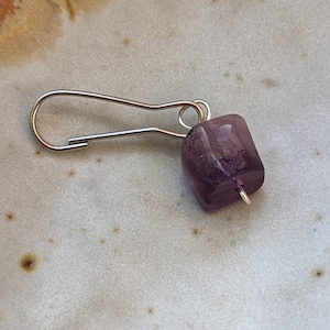 May include: A silver charm with a purple gemstone attached to a silver loop.