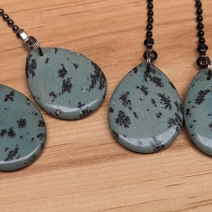 May include: Three teal blue and black teardrop-shaped pendants with black metal chains. The pendants have a speckled pattern.