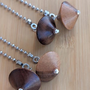 May include: Four cone-shaped wooden ceiling fan pulls attached to silver-toned metal ball chains. The pulls feature smooth, polished wood in varying shades of brown, ranging from light tan to dark espresso, each finished with a small silver metal tip.