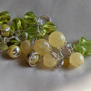 May include: A collection of green and yellow glass beads and charms, some in the shape of stars, connected by silver rings.