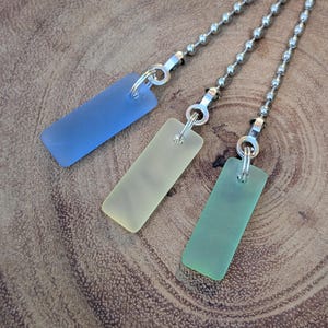 May include: Three rectangular pendants made of frosted, sea-glass-like material in shades of blue, pale yellow, and light green. Each pendant is attached to a silver-toned metal ball chain by a small jump ring, creating a set of three pull chains.