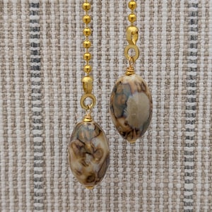 Peut inclure: Deux chaînettes de ventilateur de plafond composées de chaînes à billes en métal doré reliées à des perles ovales. Les perles présentent un motif marbré avec des tourbillons de crème, de brun et de gris foncé, fixées par des fils dorés.