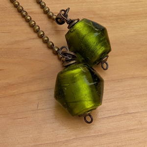 May include: Two faceted, translucent lime green glass beads attached to antique brass-toned metal ball chains. Each bead features a metallic sheen and is secured with a wire-wrapped loop and a small metal ring at the base for hanging.
