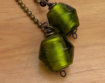 May include: Two faceted, translucent lime green glass beads attached to antique brass-toned metal ball chains. Each bead features a metallic sheen and is secured with a wire-wrapped loop and a small metal ring at the base for hanging.