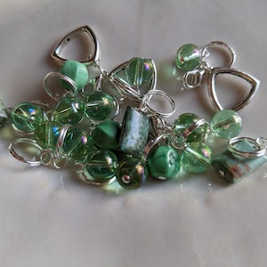 May include: A collection of green glass beads, green stone beads, and silver bead caps. The beads are strung together on a silver chain.