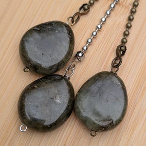 May include: Three polished, dark olive-green, irregular, rounded stone pendants attached to metal ball chains. Two of the stones are connected to antique bronze-toned chains, while one is attached to a silver-toned metal ball chain.