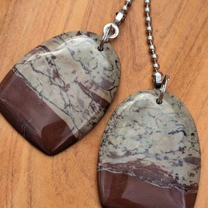 May include: Two brown and white stone pendants with a silver chain. The stones have a layered pattern with brown, white, and gray colors.