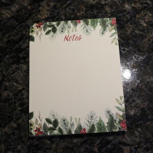 May include: A white notepad with a green and red holly border. The notepad has the word "Notes" written in red at the top.