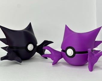May include: Two 3D printed figures of a Pokemon character, one in purple and one in black. Both figures have a white and black Pokeball design on their bellies.