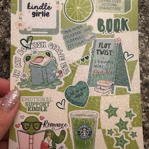 May include: A green and white sticker sheet featuring book-related designs and text. Illustrations include a frog reading, a Starbucks coffee cup, and phrases such as "Book Nerd" and "Plot Twist: I bought more books."