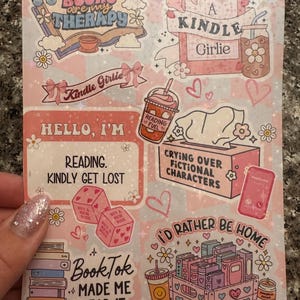 May include: A pink and white sticker sheet with various book-themed illustrations and text. The stickers feature phrases like "Books are my therapy", "Kindle Girlie", "Reading. Kindly get lost", "Crying over fictional characters", "I'd rather be home", and "BookTok made me read it".