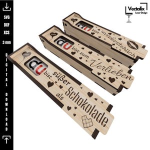 Può includere: Tre scatole di legno con disegni tagliati al laser, ognuna contenente una leccornia al cioccolato. Le scatole presentano testo in tedesco, tra cui "bist süßer als Schokolade" e "bist zum Verlieben." Sono presenti anche motivi a cuore e barretta di cioccolato.