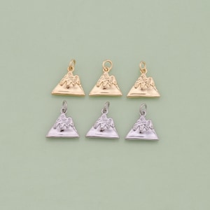 May include: Six gold and silver mountain charm pendants. The charms are in the shape of a mountain with a textured surface. The charms are perfect for adding a touch of nature to your jewellery.