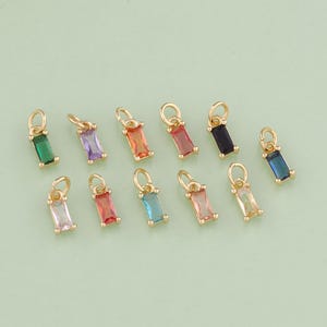 May include: Assortment of 10 gold charm pendants with colorful rectangular gemstones. The charms feature a variety of colors including green, purple, pink, orange, blue, and black.