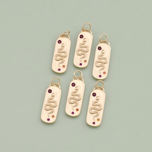 May include: Six gold-colored rectangular pendants with a snake design. Each pendant features a coiled snake, a red gem, and an orange gem. The pendants have a loop at the top for attaching to a chain or bracelet.