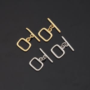 May include: Two pairs of metal toggle clasps, one pair in gold and one pair in silver. Each clasp has a rectangular loop and a straight bar.
