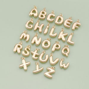 May include: A set of 26 gold-colored alphabet letter charms. Each letter is in a bubble-like font style.