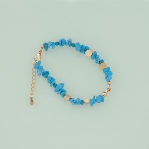May include: A delicate bracelet featuring turquoise-colored stone chips and gold-colored metal accents. The bracelet has a gold-colored chain and clasp for adjustable sizing. The stones are irregularly shaped, adding a unique touch to the jewelry.
